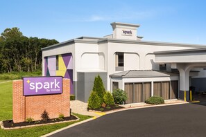 Exterior de un hotel con un cartel que dice 'spark by Hilton', una entrada de ladrillo y un área de estacionamiento.