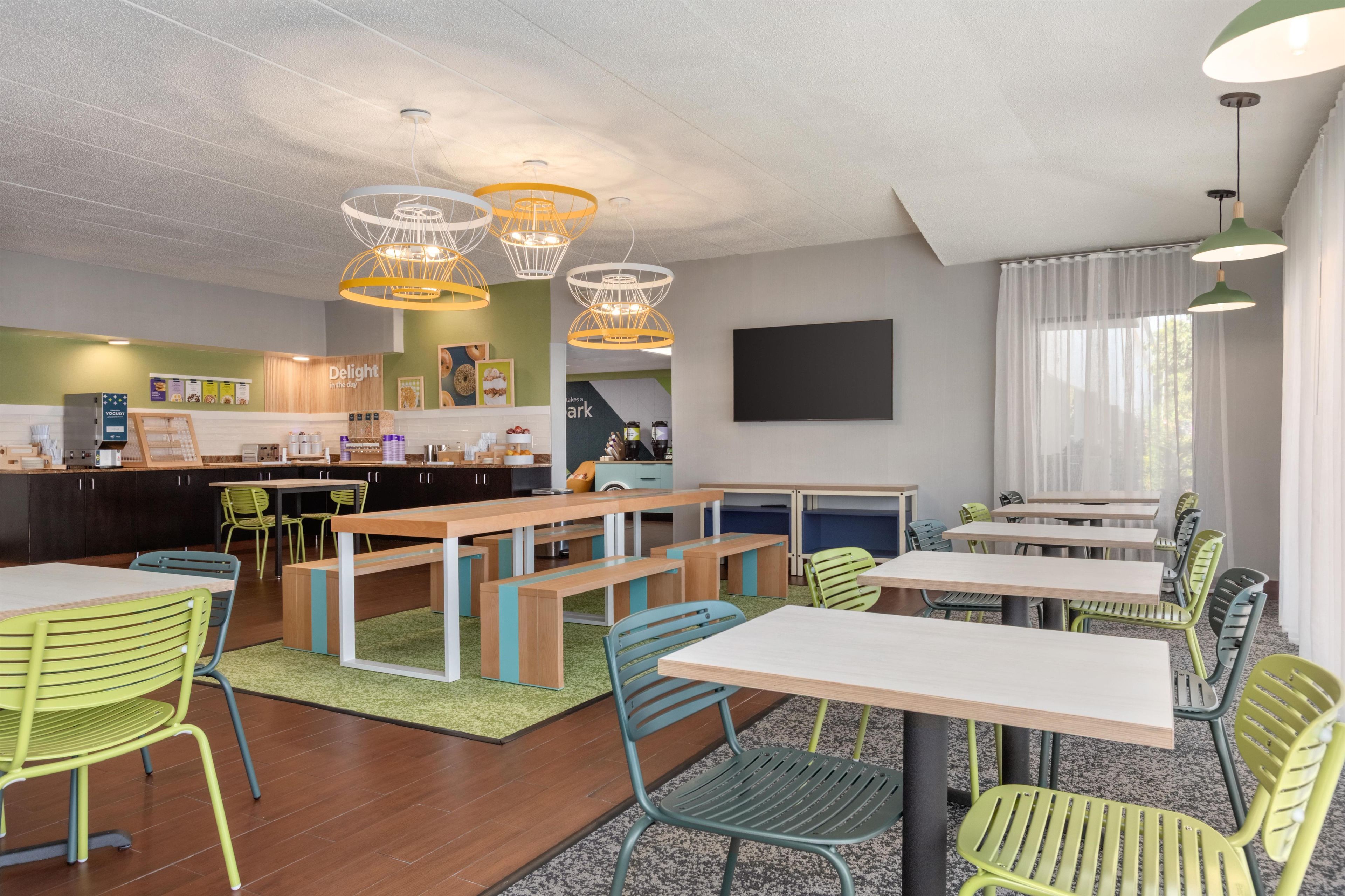 A modern dining area with multiple tables and chairs, a counter with food items, and a television mounted on the wall.