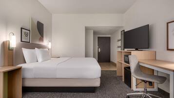 Una habitación de hotel con cama, escritorio, silla, televisión y obras de arte en las paredes.