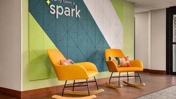 A modern lobby with two rocking chairs, a geometric wall design, and a sign that reads 'It only takes a spark'.