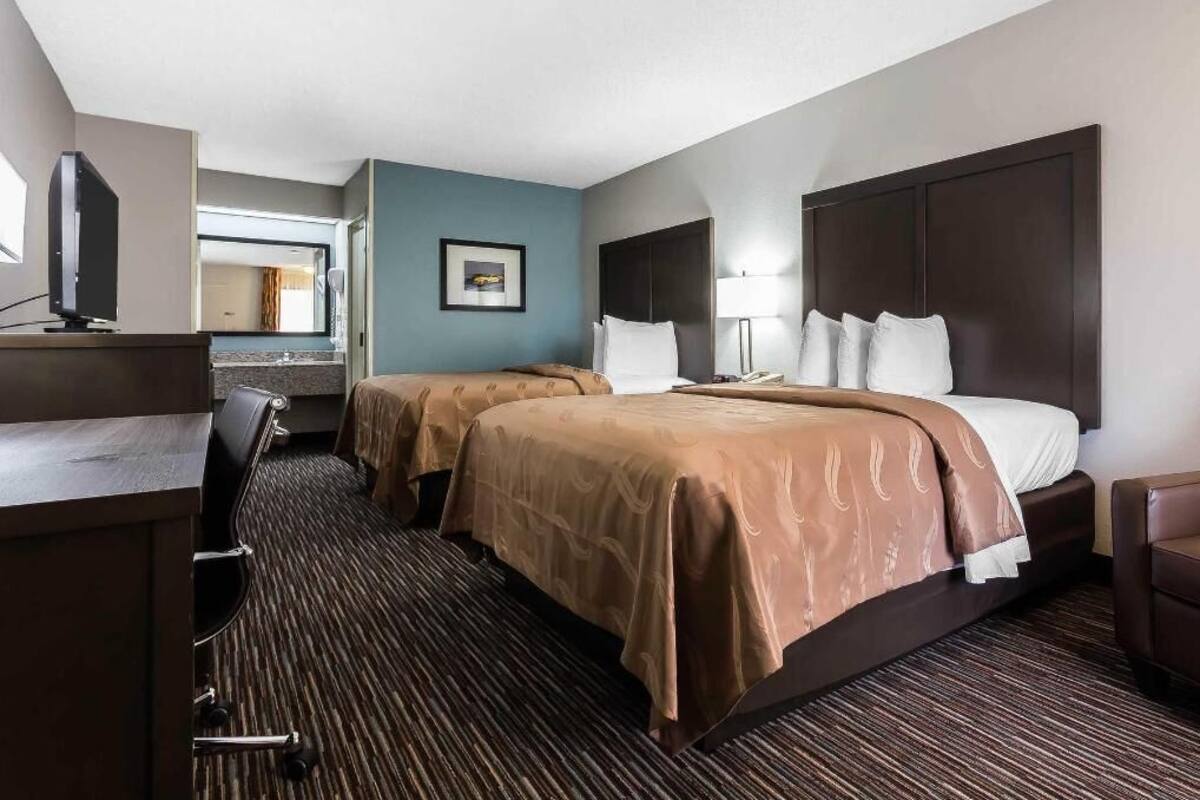 Ein Hotelzimmer mit zwei Betten, einem Schreibtisch, einem Sessel, einem Fernseher und einem Bild an der Wand.