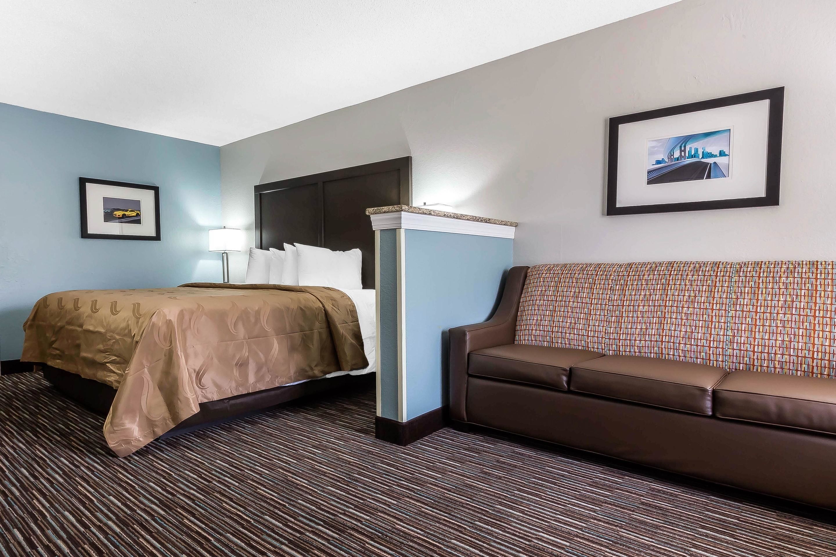 Ein Hotelzimmer mit Bett, Sofa, Schreibtisch und einem gerahmten Bild an der Wand.
