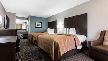 A hotel room with two beds, a desk, a chair, and a TV.