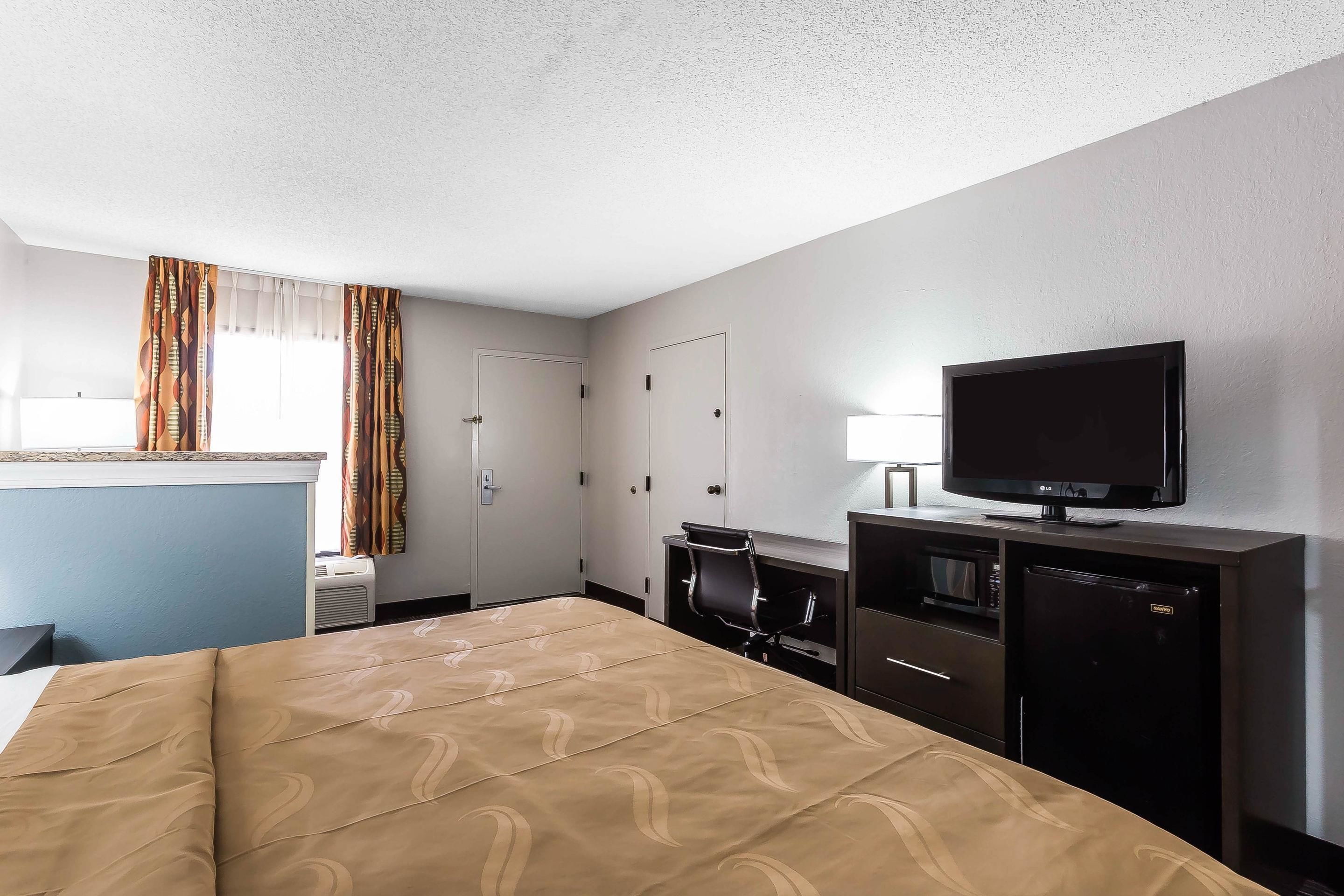 A hotel room with a bed, a desk with a chair, a television, a microwave, and a refrigerator.
