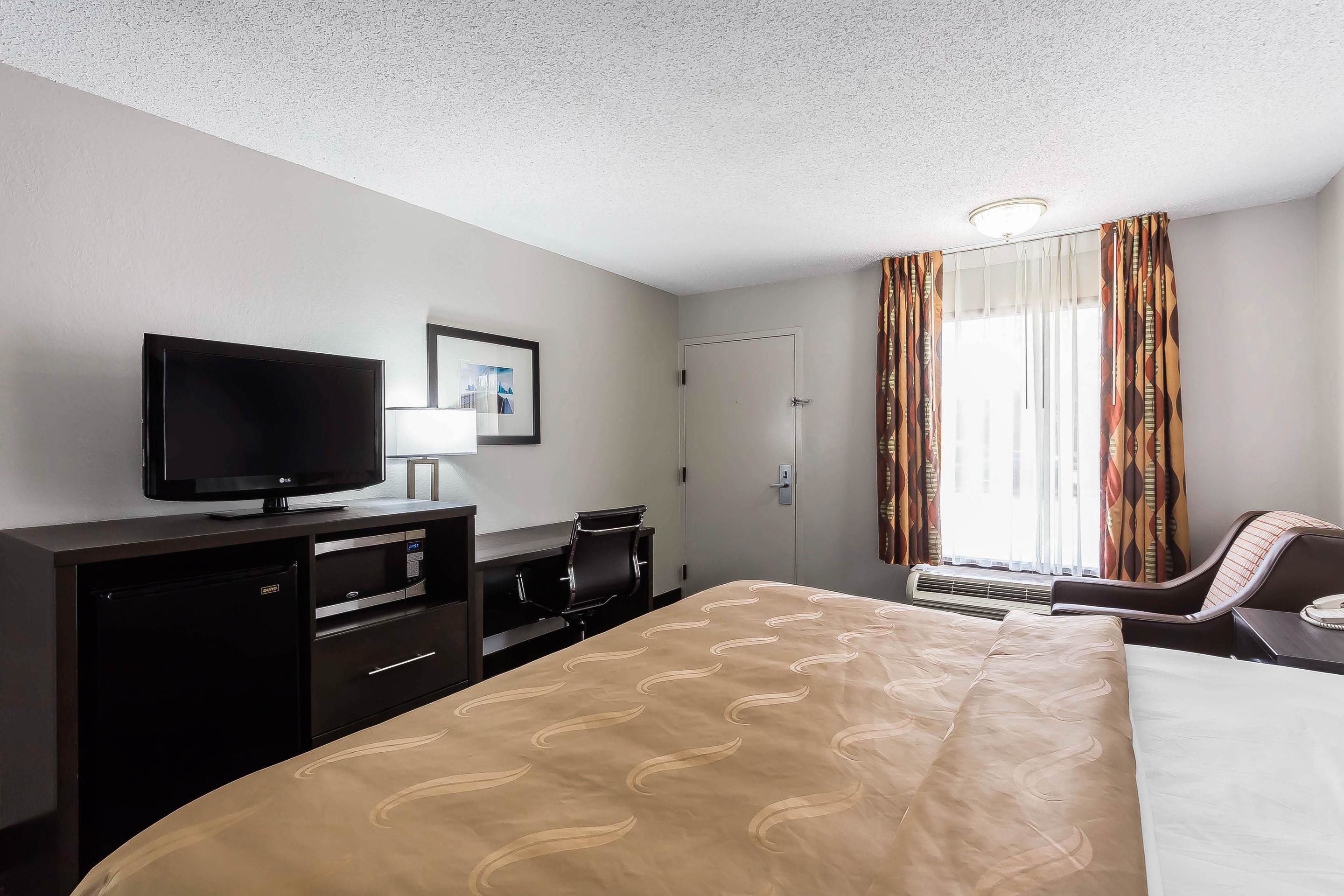 Habitación de hotel con una cama, televisor, escritorio y una silla.