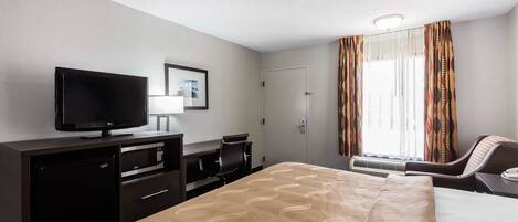 Habitación de hotel con una cama, televisor, escritorio y una silla.