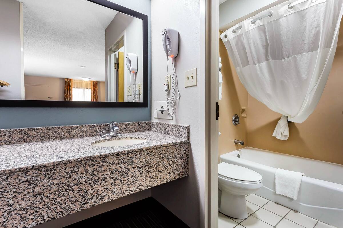 Ein Badezimmer mit einer Granit-Arbeitsplatte, einem an der Wand montierten Fön, einer Toilette und einer Badewanne mit weißer Duschvorhang.