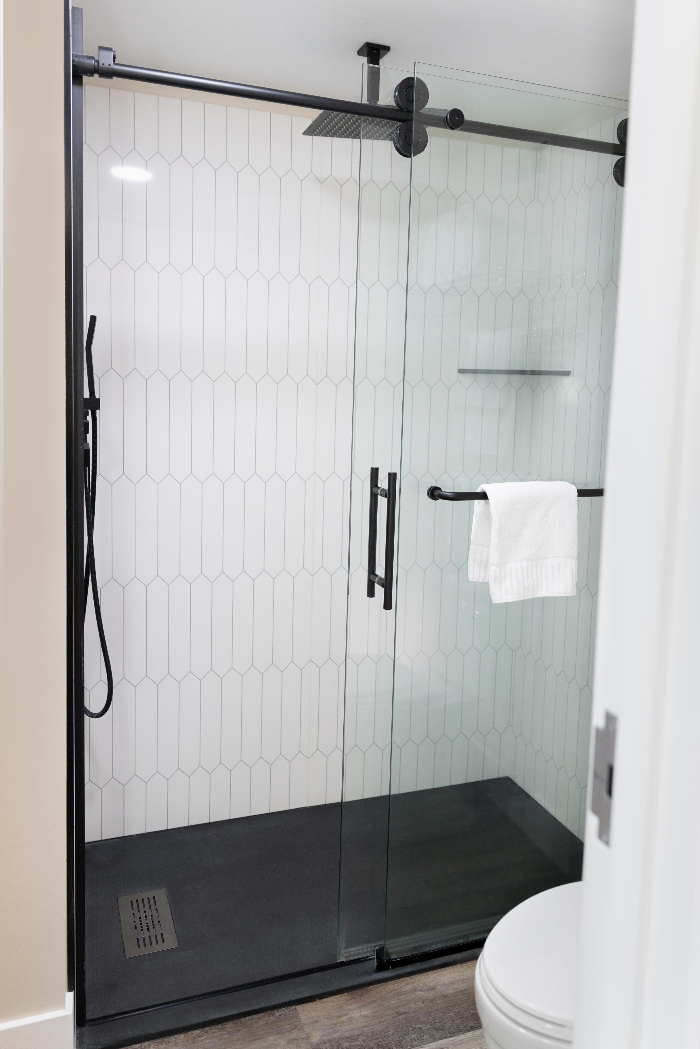 A glass-enclosed shower with a black handle and a towel rack.