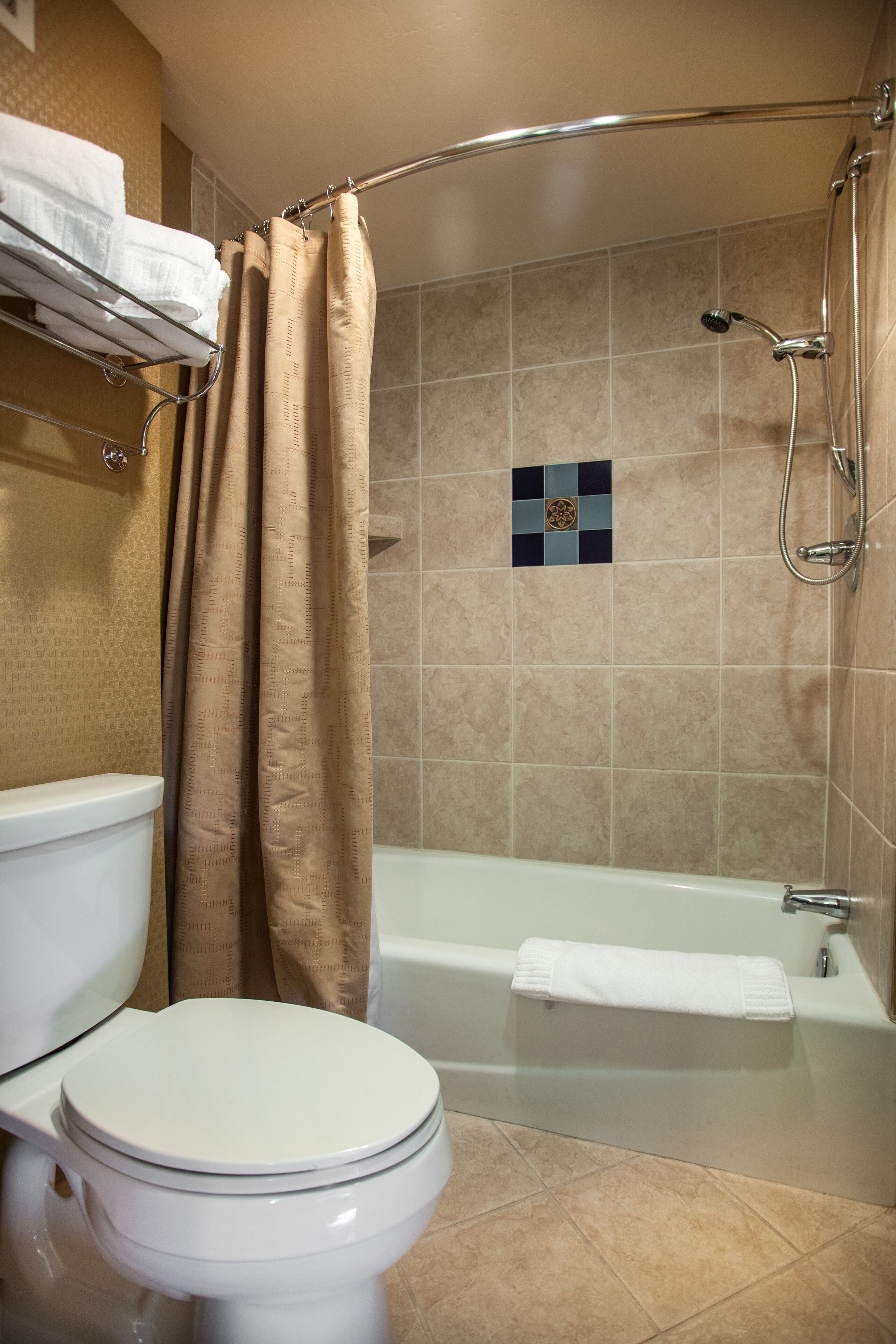 A bathroom with a toilet, bathtub, shower, and beige tiled walls.