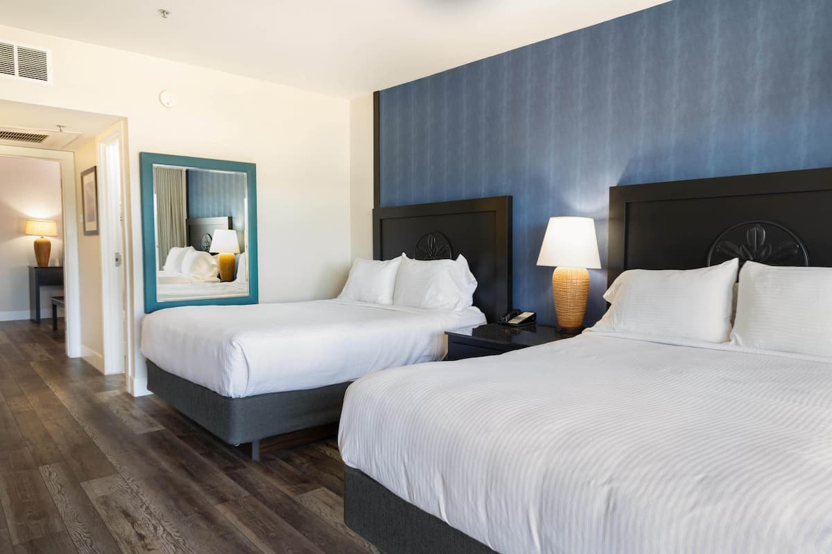 A hotel room with two beds, a mirror, bedside lamps, and a wooden floor.
