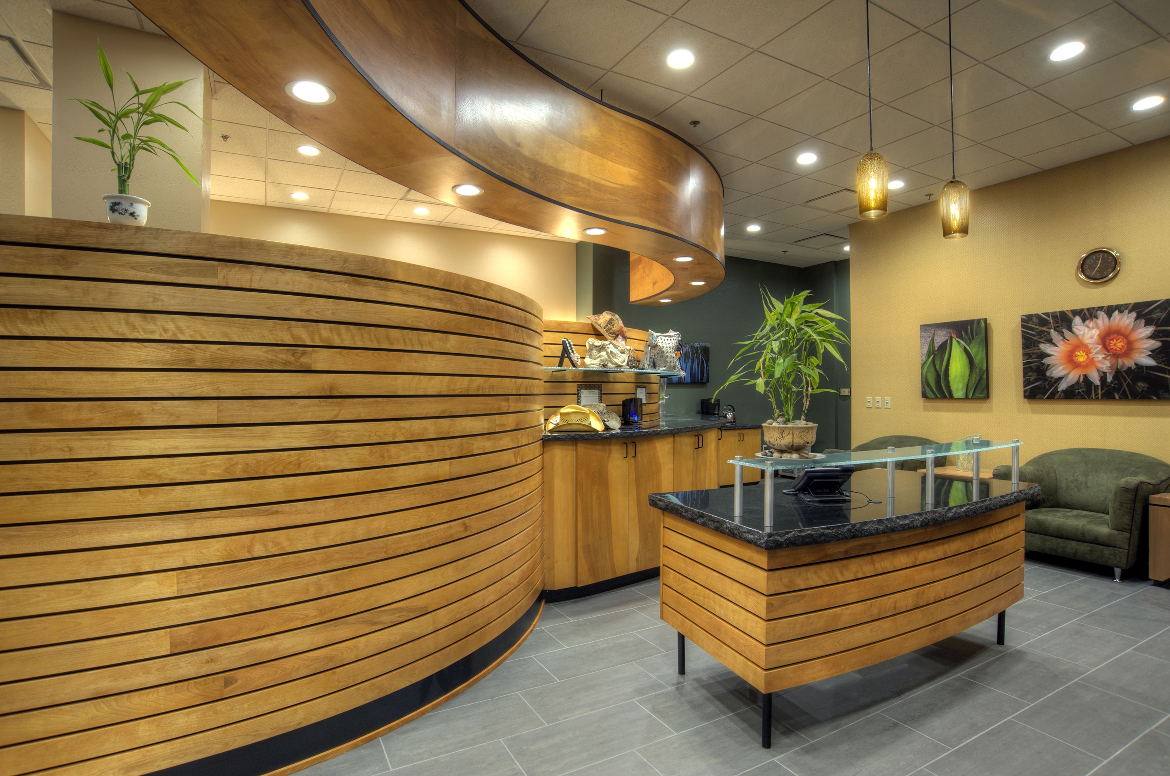 Un espace d’accueil doté d’un comptoir de réception en bois aux lignes courbes, d’une cloison en verre et d’un canapé vert.