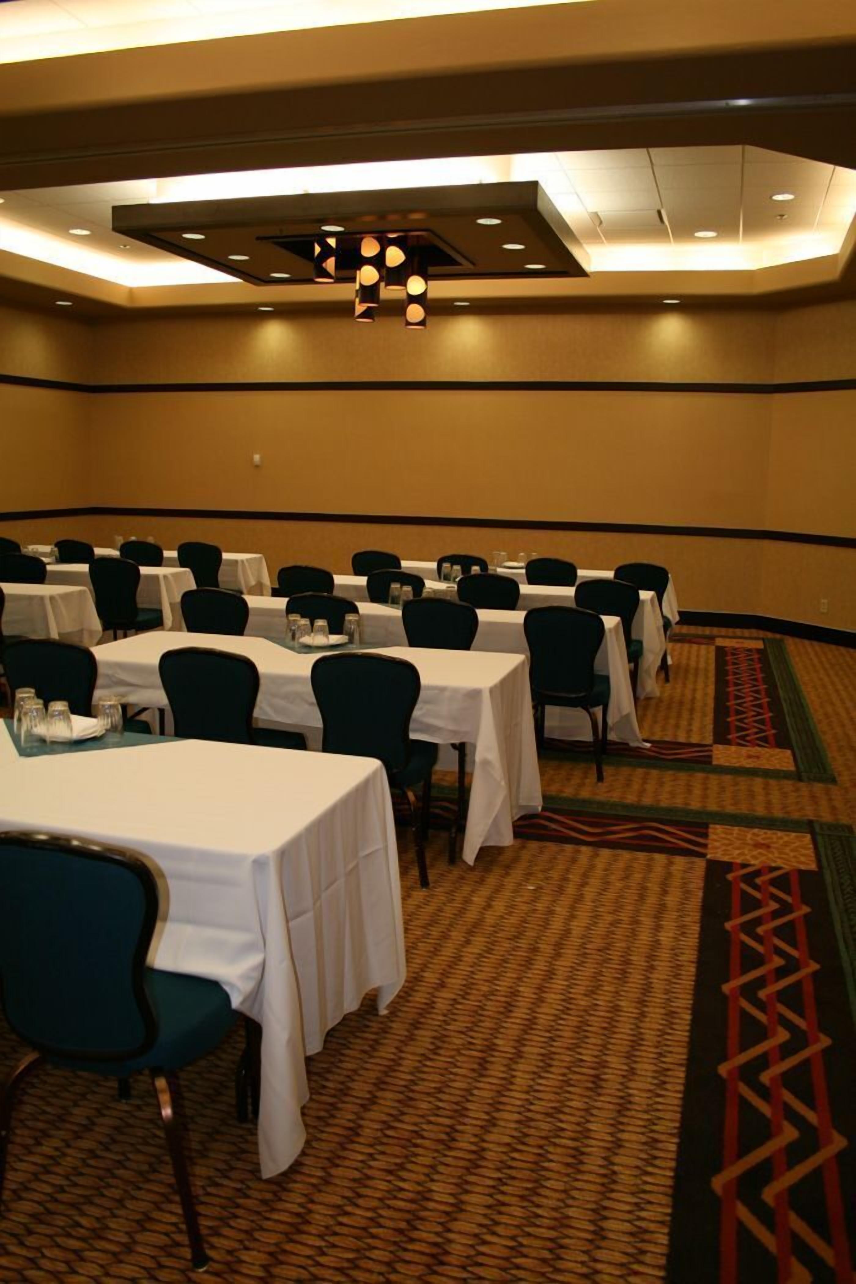 Un salón de conferencias con varias mesas y sillas, suelo alfombrado e iluminación empotrada.