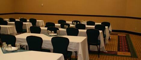 Un salón de conferencias con varias mesas y sillas, suelo alfombrado e iluminación empotrada.