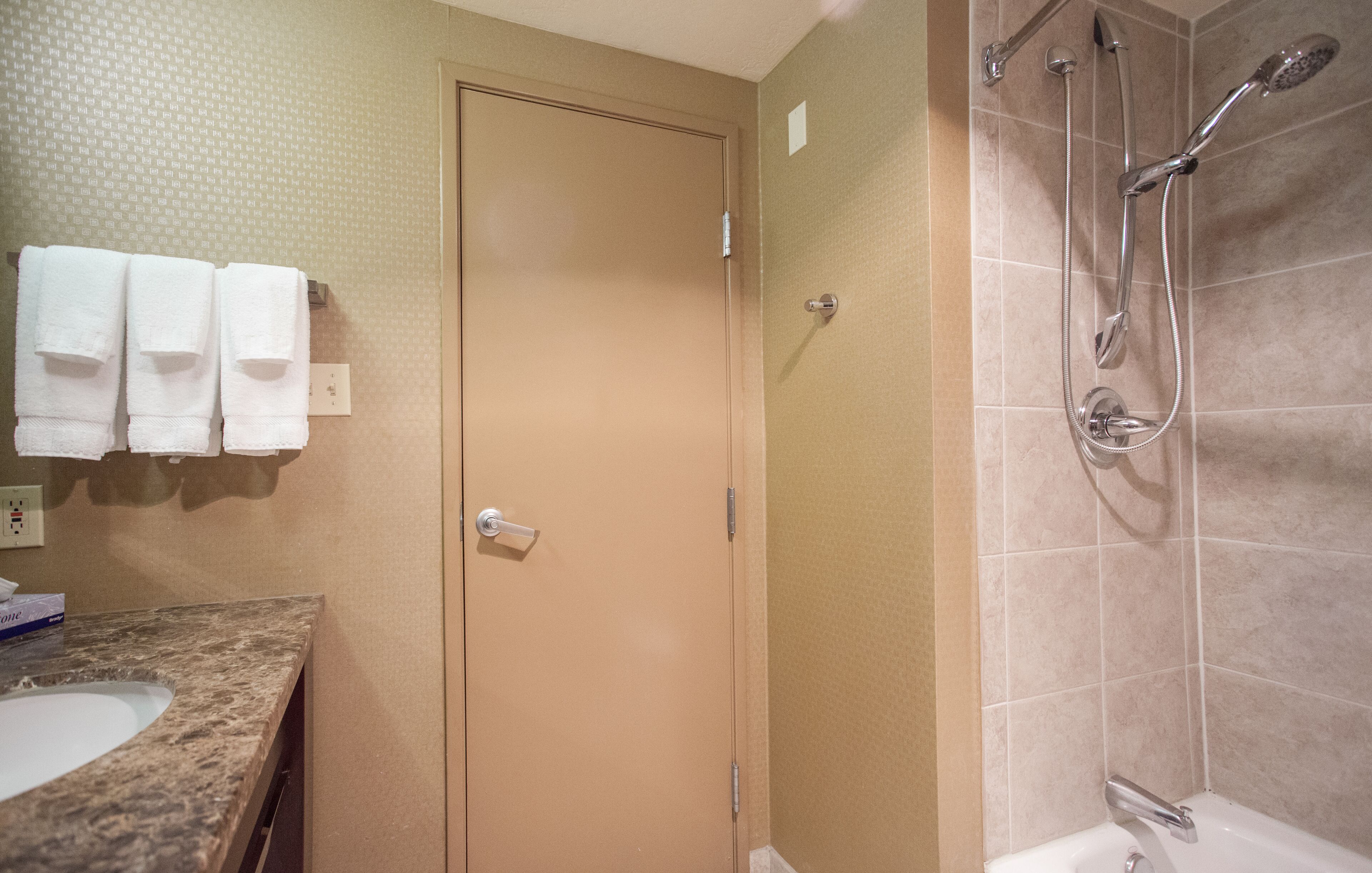 A bathroom with a shower, a sink, and three towels hanging on the wall.