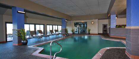 An indoor swimming pool with a clear view of the pool area, lounge chairs, and potted plants.