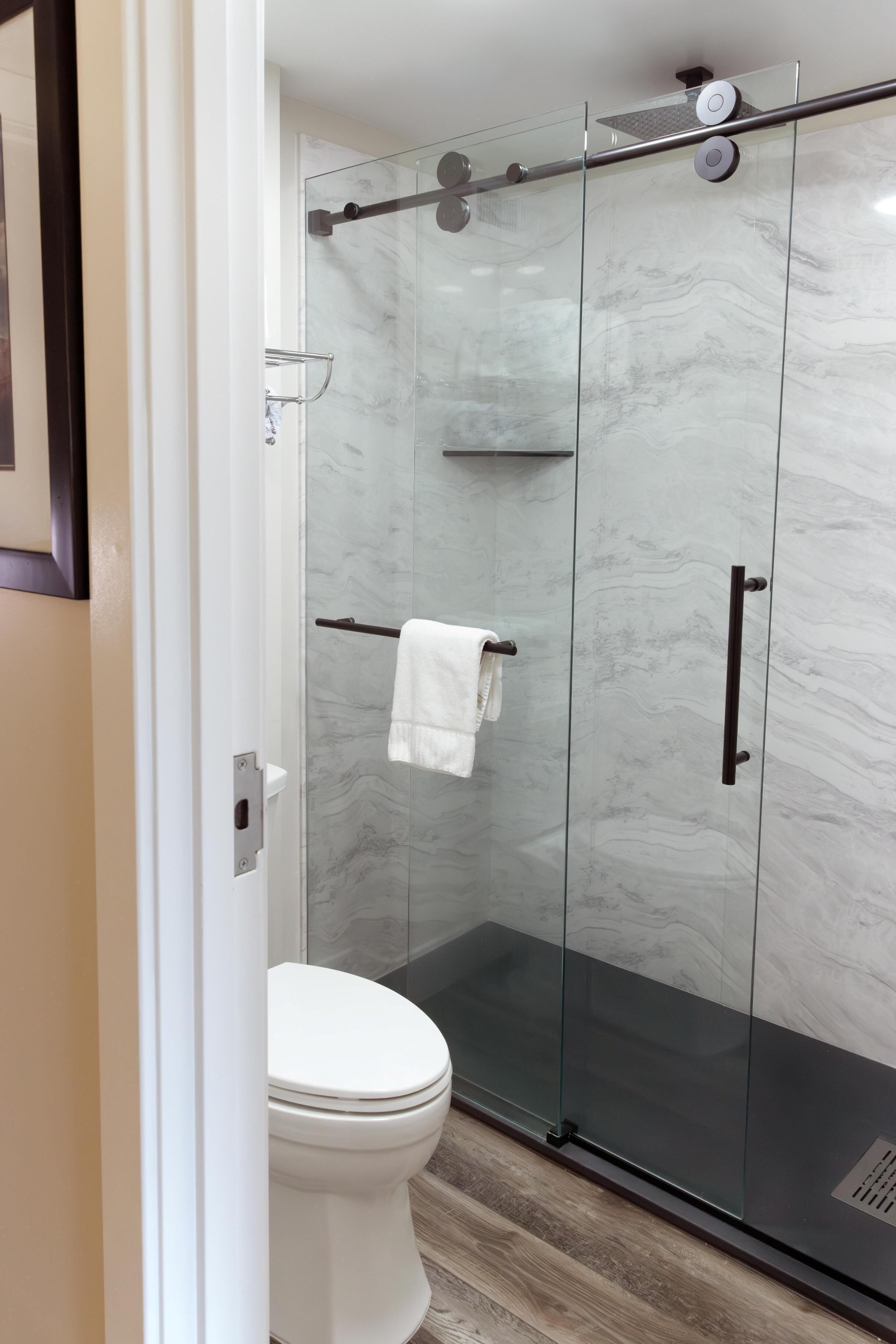 Un baño moderno con ducha de vidrio, inodoro blanco y pared de mármol.