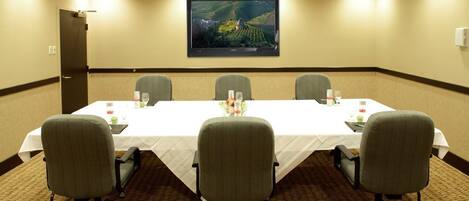 Un salón de conferencias con una larga mesa, cuatro sillas y una pantalla grande en la pared.