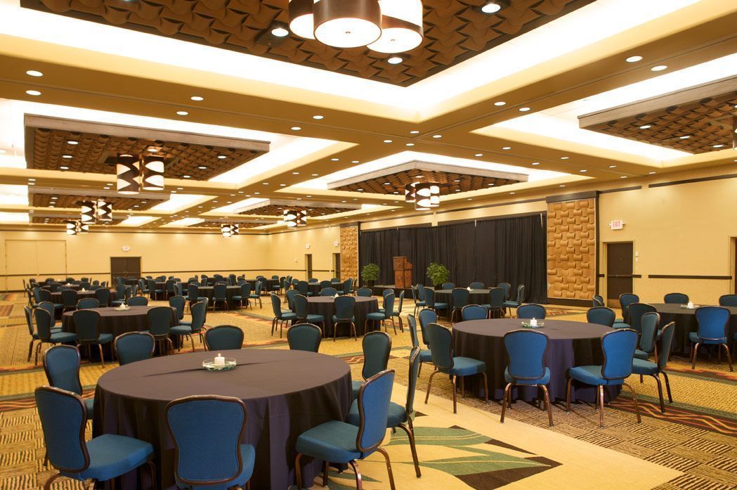 A large conference room with multiple round tables and chairs, arranged in rows.