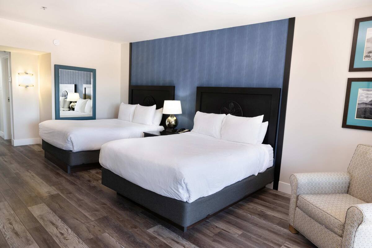 A hotel room with two beds, a chair, a nightstand, and a mirror.