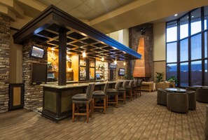 A bar area with a stone wall, multiple bar stools, a television, and a large window offering a view. - Prescott Resort and Conference Center (Prescott)