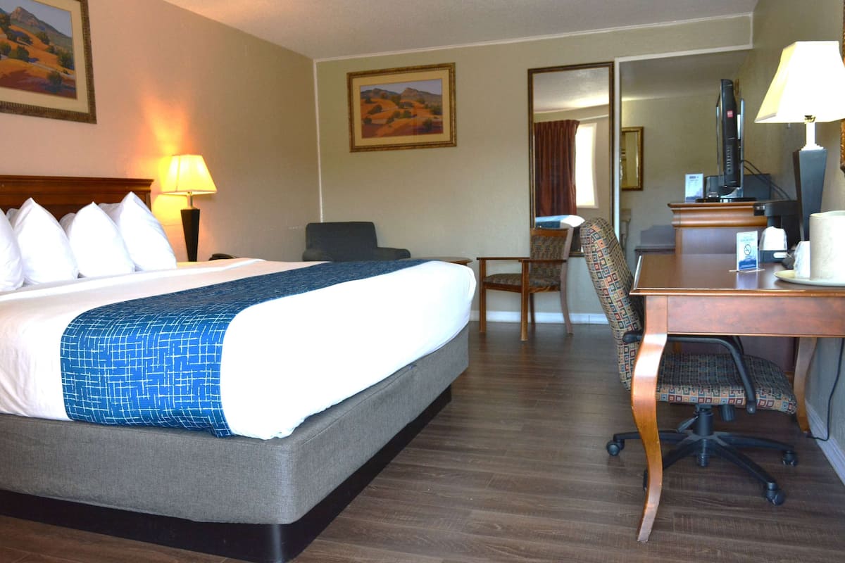 A hotel room with a large bed, a desk with a chair, a television, and a mirror.