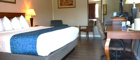 A hotel room with a large bed, a desk with a chair, a television, and a mirror.
