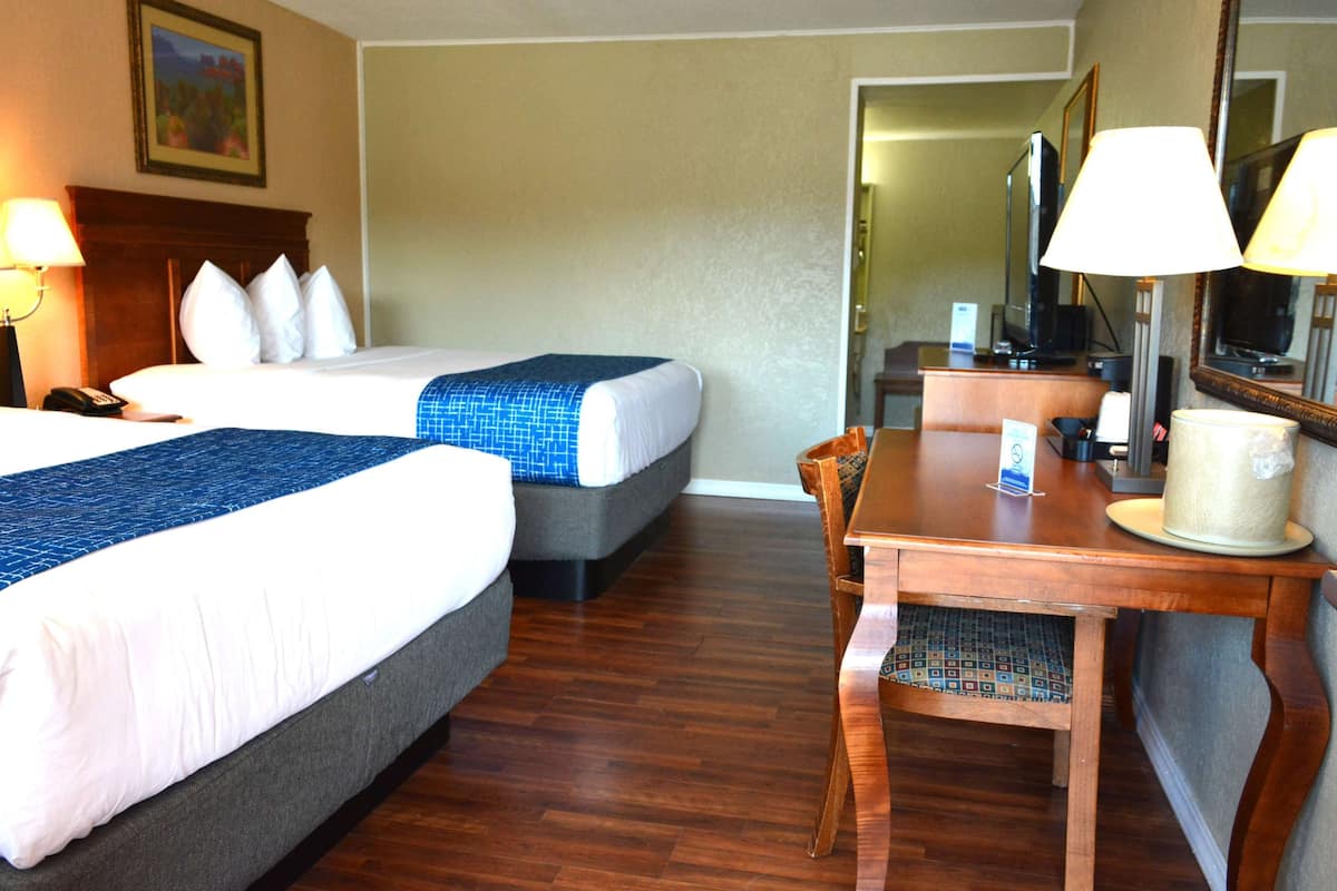 A hotel room with two beds, a wooden desk, a chair, a lamp, a television, and a mirror.