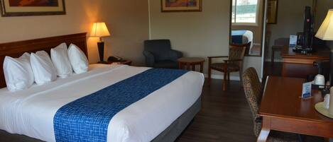 A hotel room with a large bed, a desk, a chair, and a small table.