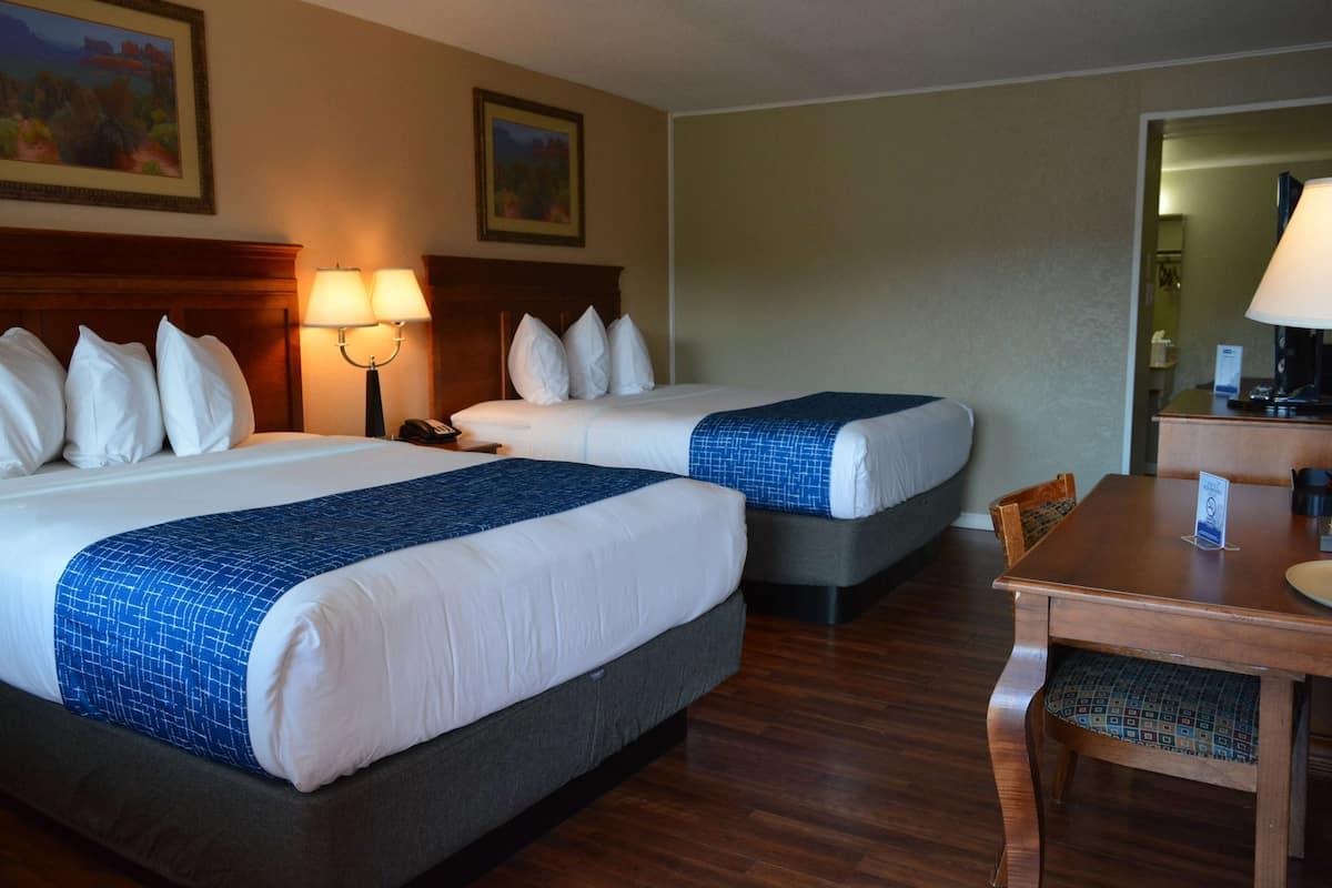 A hotel room with two beds, a wooden desk, and a chair.