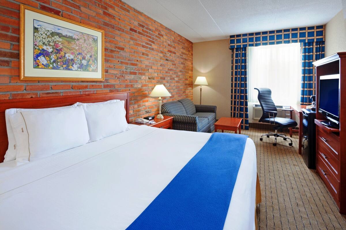 A hotel room with a large bed, a desk with a chair, a television, and a painting on the wall.