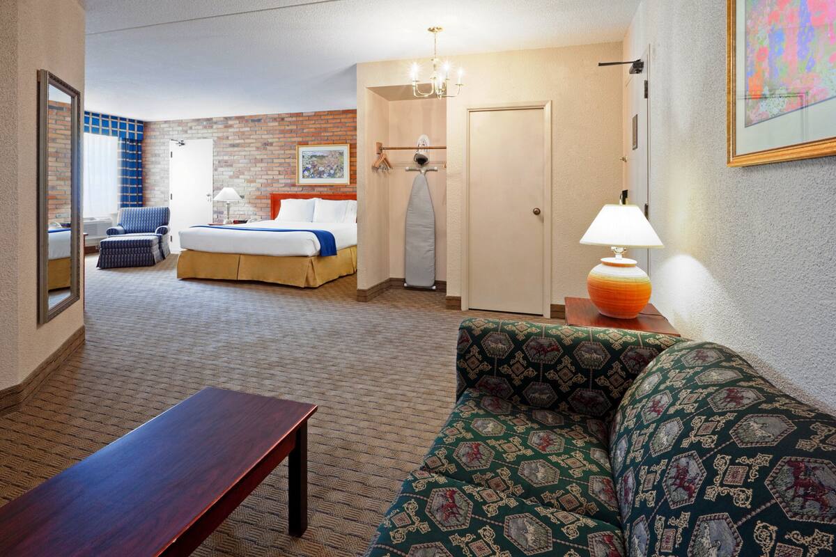 A hotel room with a bed, a sofa, a table, a mirror, a chandelier, and a door.