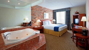 Et hotelværelse med et stort badekar, en seng med et blåt lagen, et skrivebord med en lampe og et fjernsyn.