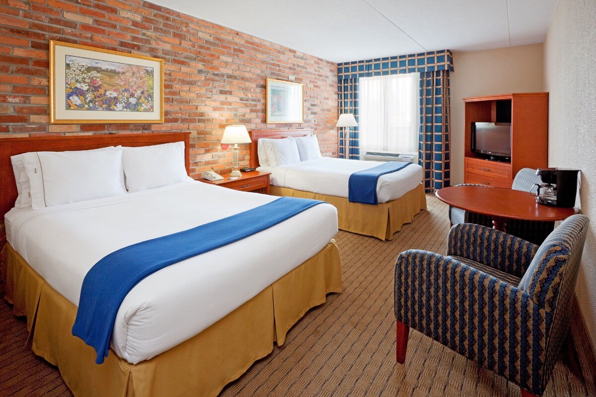 A hotel room with two beds, a TV, a desk, and a chair.