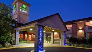 Et Holiday Inn Express-hotel med et markant tårn-skilt, parkeringsområde under tag og en veloplyst indgang.