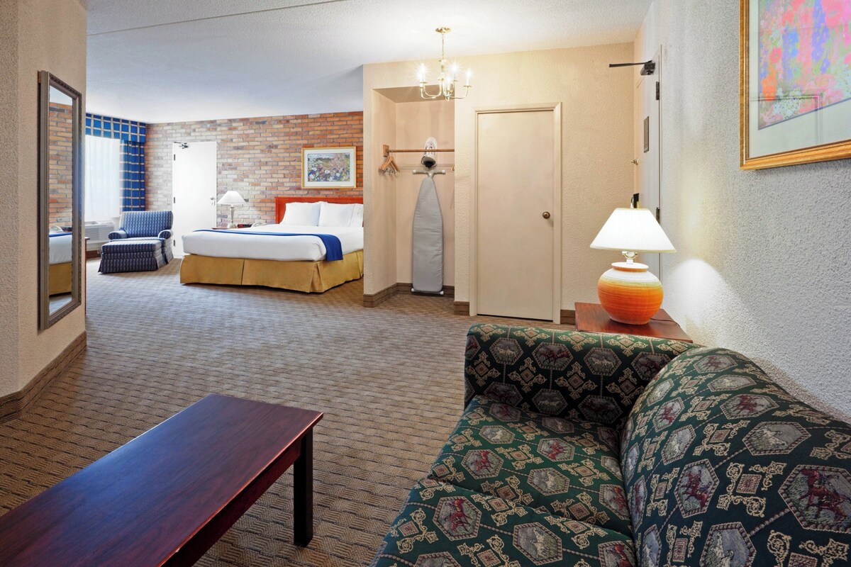 A hotel room with a bed, a sofa, a table, a mirror, a chandelier, and a door.