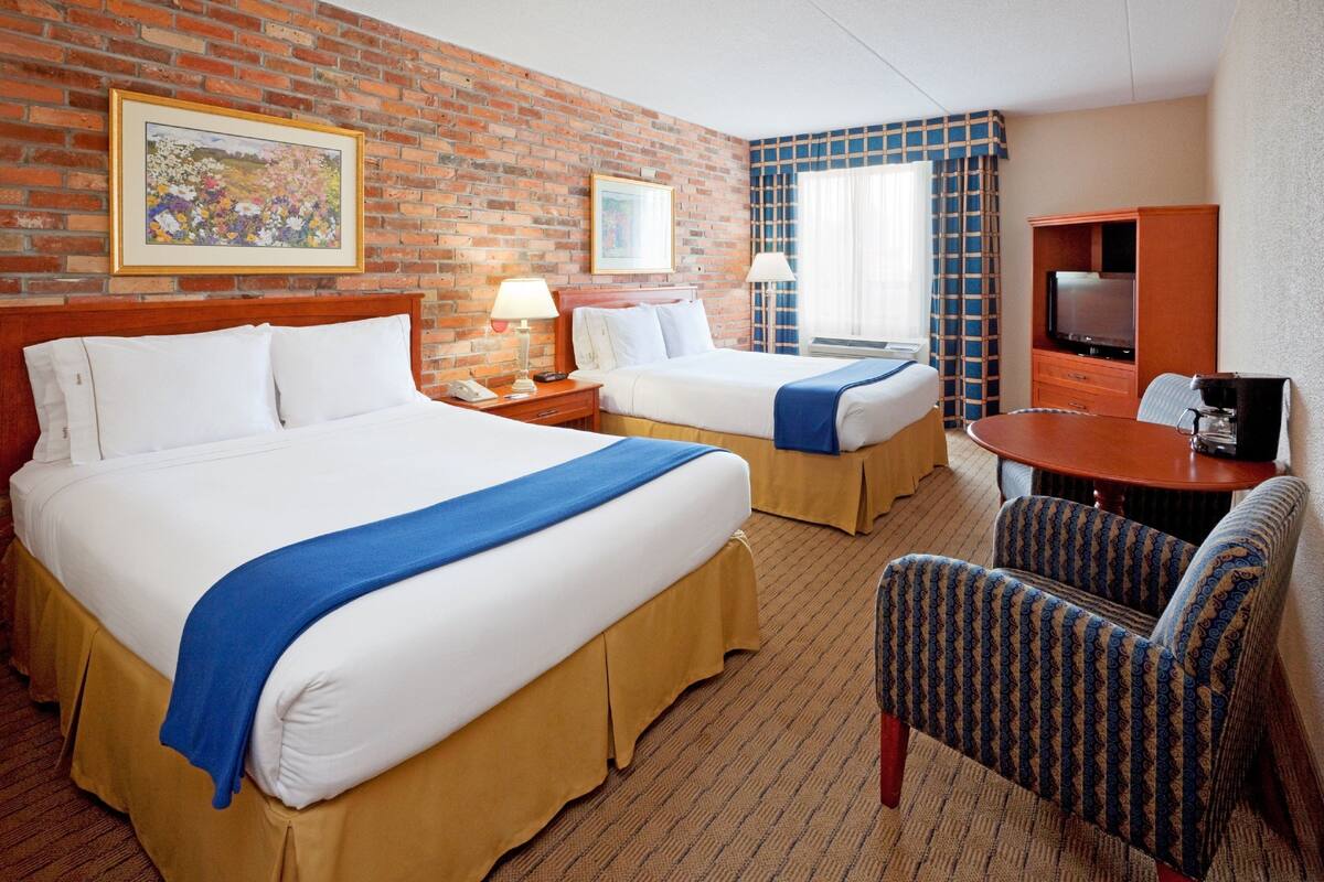 A hotel room with two beds, a TV, a desk, and a chair.