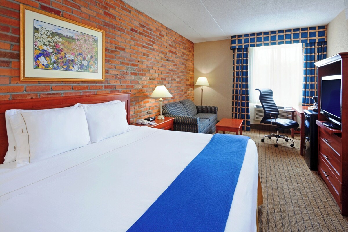 A hotel room with a large bed, a desk with a chair, a television, and a painting on the wall.