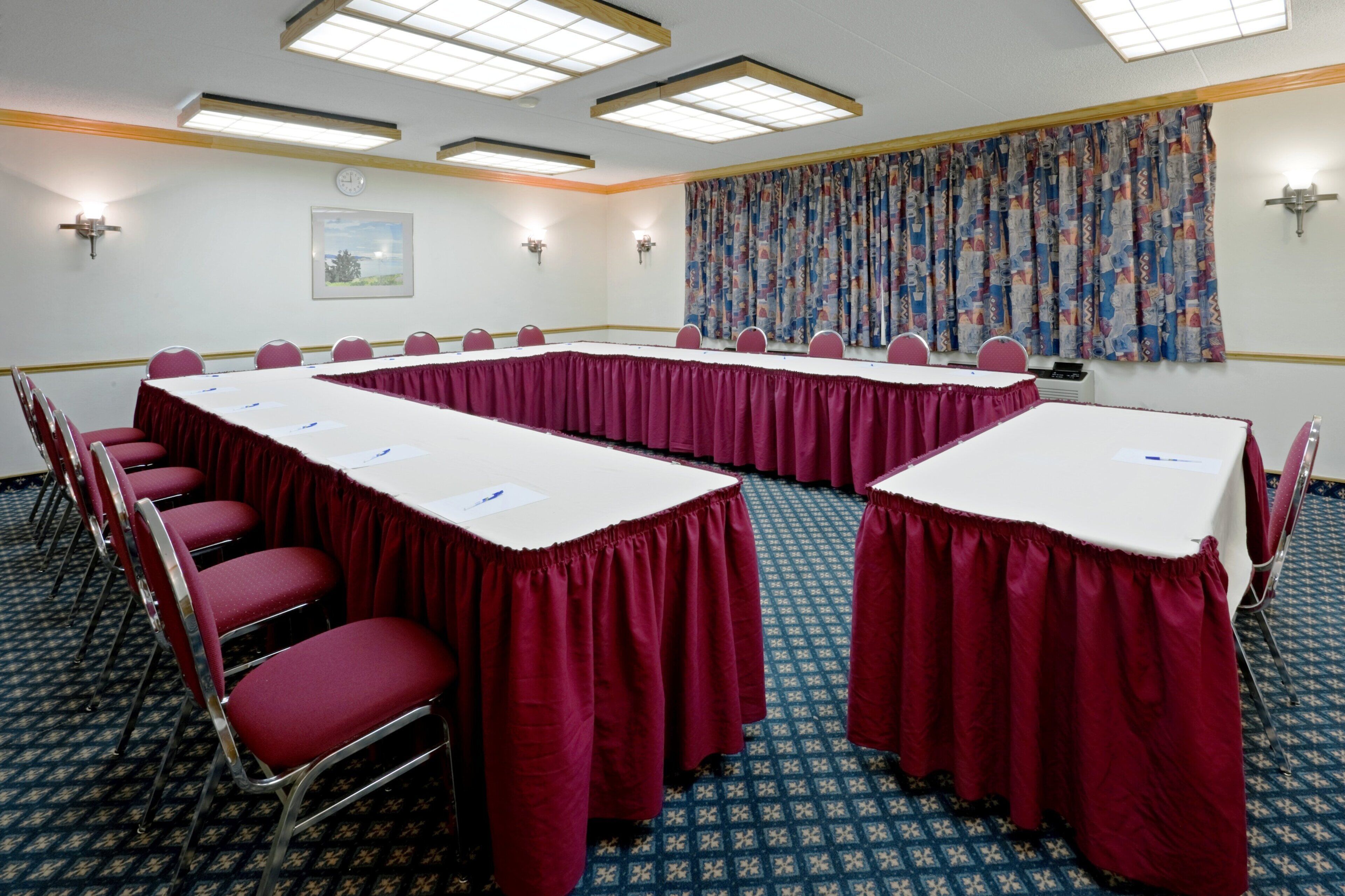 A conference room with two long tables, red chairs, and patterned carpet.