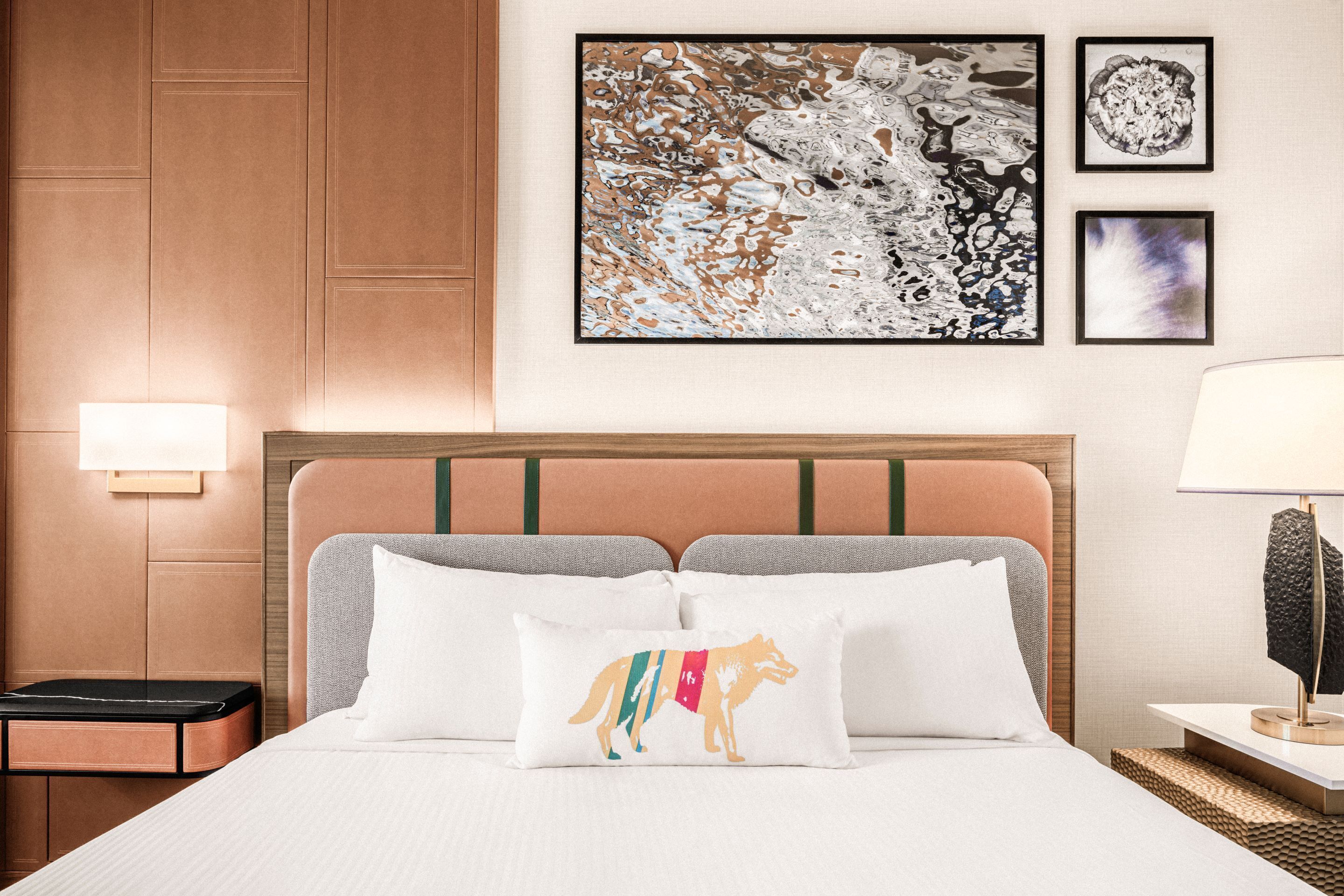 Una cama bien tendida con un cojín blanco de diseño con animales coloridos, un cabecero con un detalle verde y una pared con arte abstracto y un cuadro enmarcado.