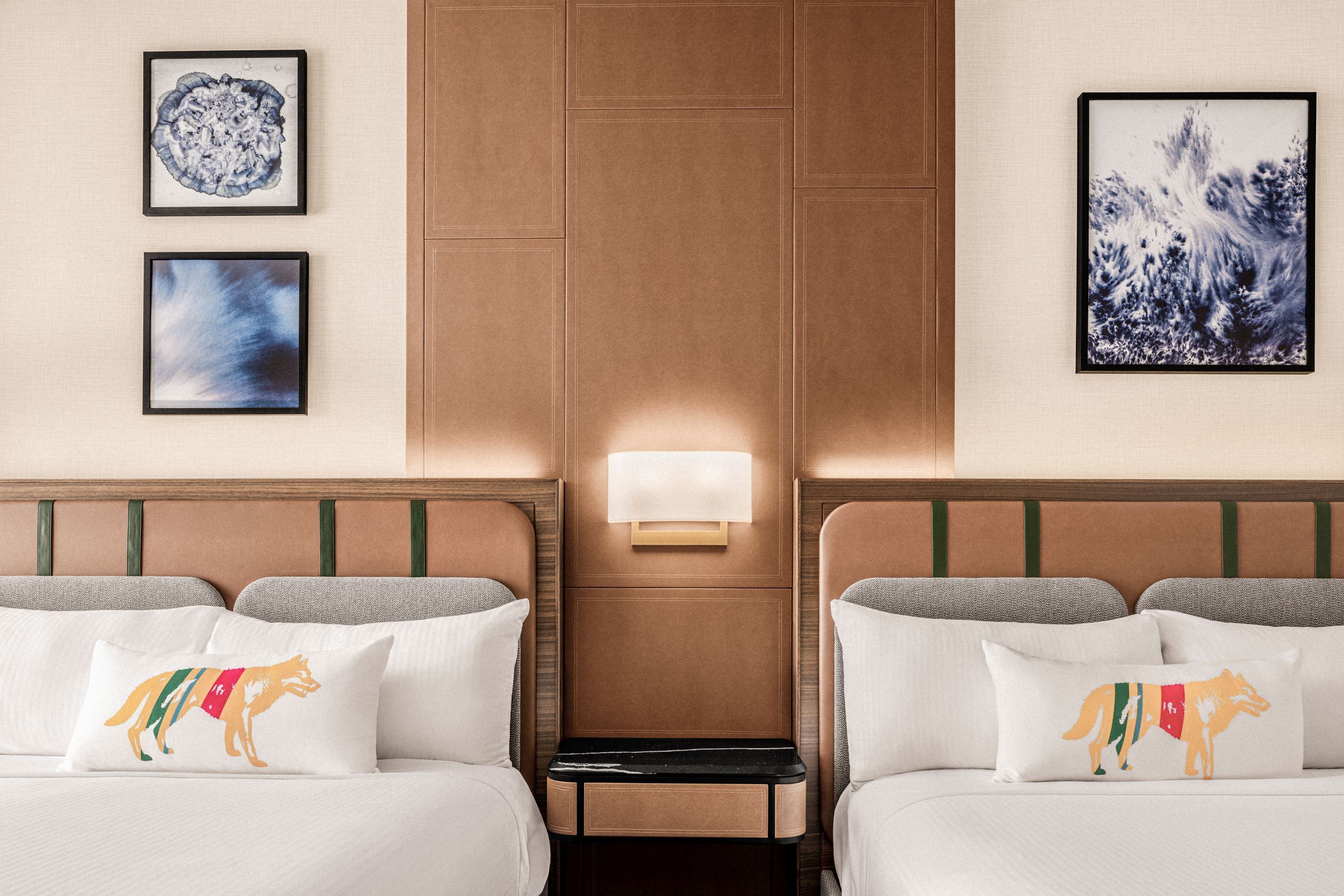 Habitación de hotel con dos camas, una mesita de noche y obras de arte colgadas en la pared.