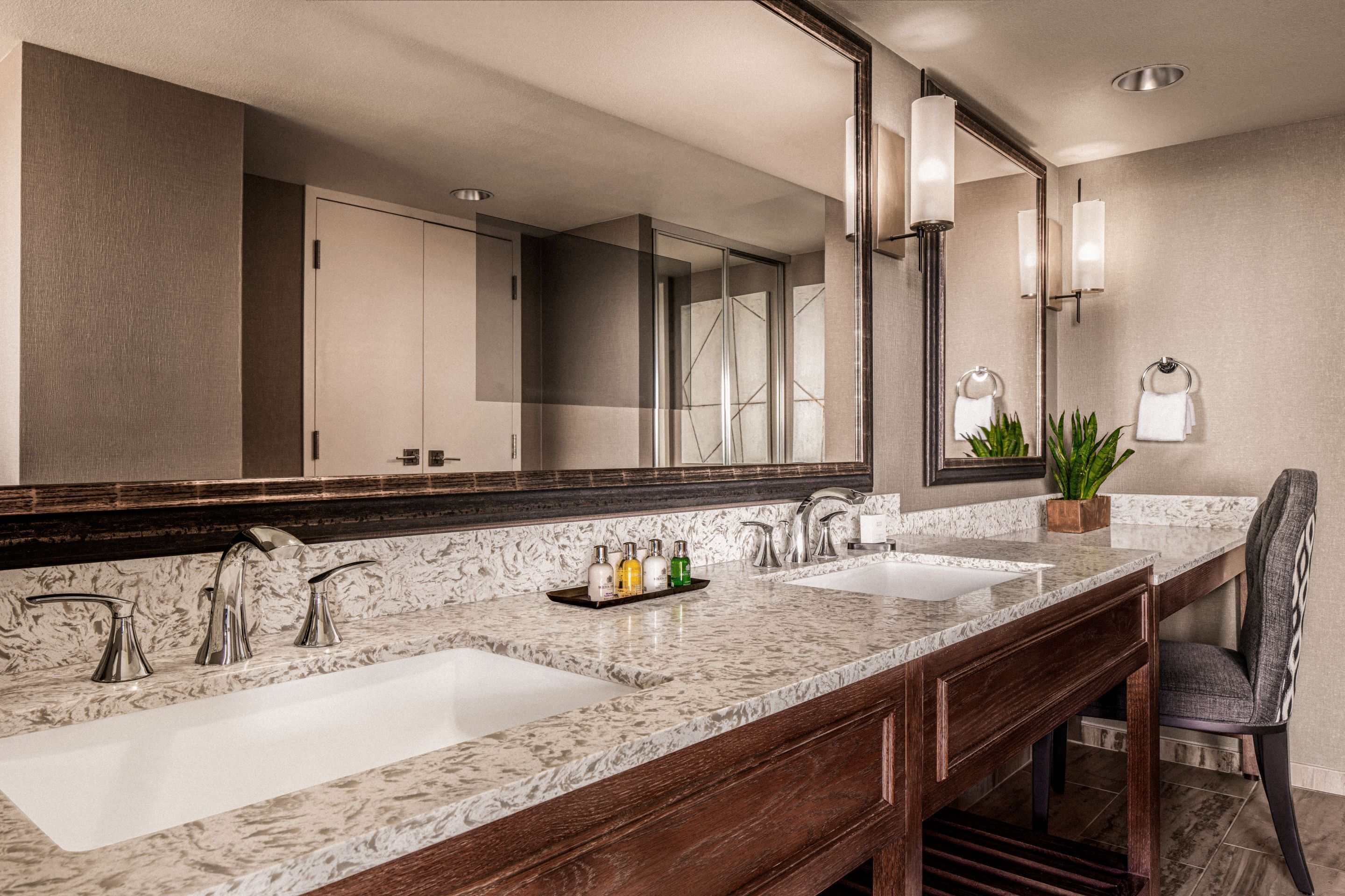 A bathroom with two sinks, a large mirror, and a chair.