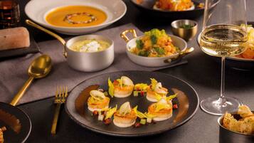 A dining table with various dishes, including a bowl of soup, a plate of scallops, and a glass of wine.