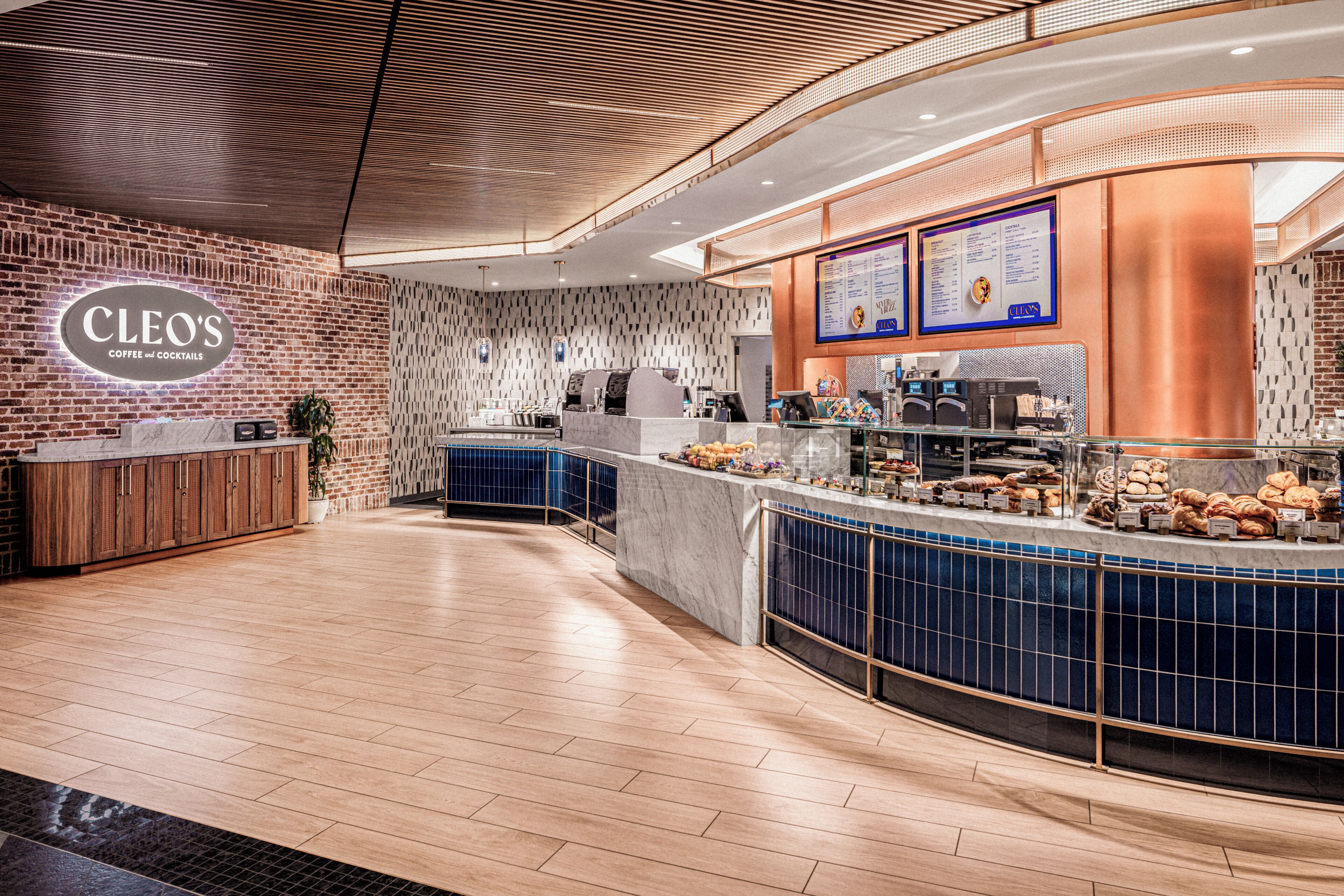 A modern coffee shop interior with a brick wall, a counter with a menu board, and a variety of baked goods.