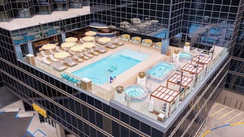 A rooftop pool area with multiple swimming pools, sun loungers, and a bar area.