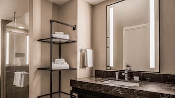 A modern bathroom with a glass shower enclosure, a black metal towel rack, a marble countertop, and a large mirror.