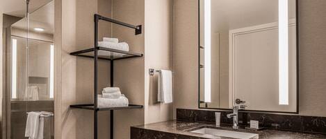Un baño moderno con cabina de ducha de vidrio, un toallero de metal negro, encimera de mármol y un espejo grande.