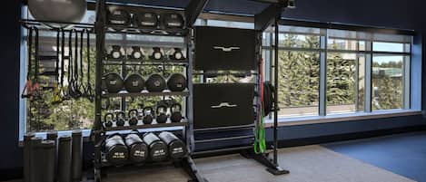 Un gimnasio con equipamiento de levantamiento de pesas, kettlebells y mancuernas.