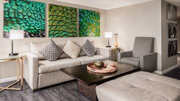 A modern living room with a sofa, armchair, coffee table, and artwork on the wall.