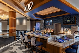 Zona de bar moderna con pantalla digital, taburetes y una variedad de botellas de licor.