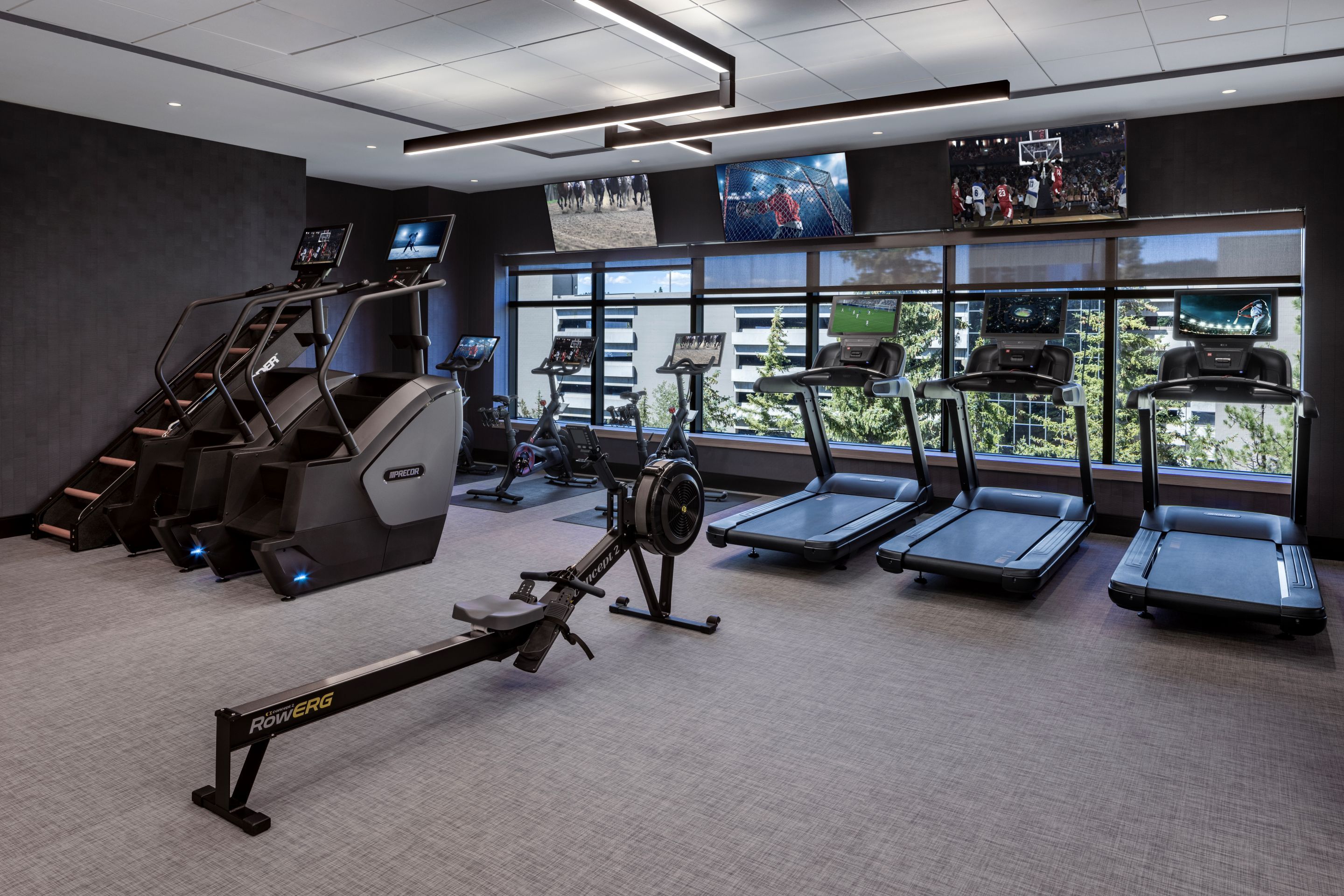 Une salle de sport équipée de tapis de course, d’un appareil d’aviron et d’un simulateur de marche en escalier.